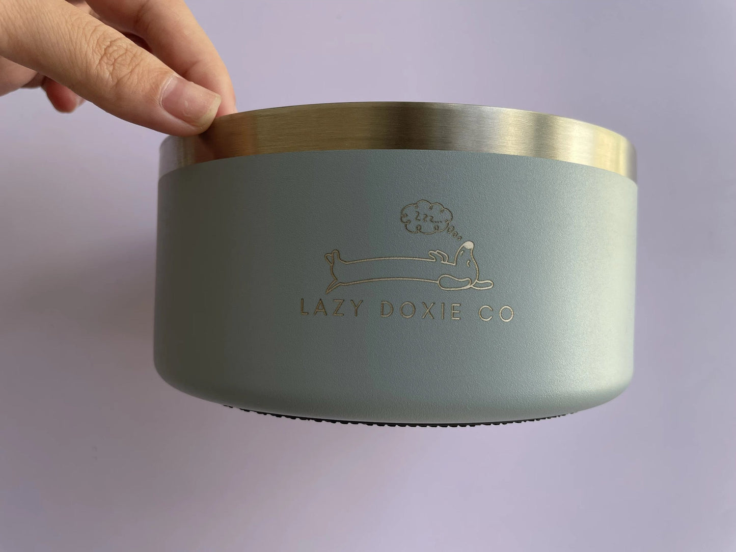 Light green container with gold lid held by a hand on a light purple background